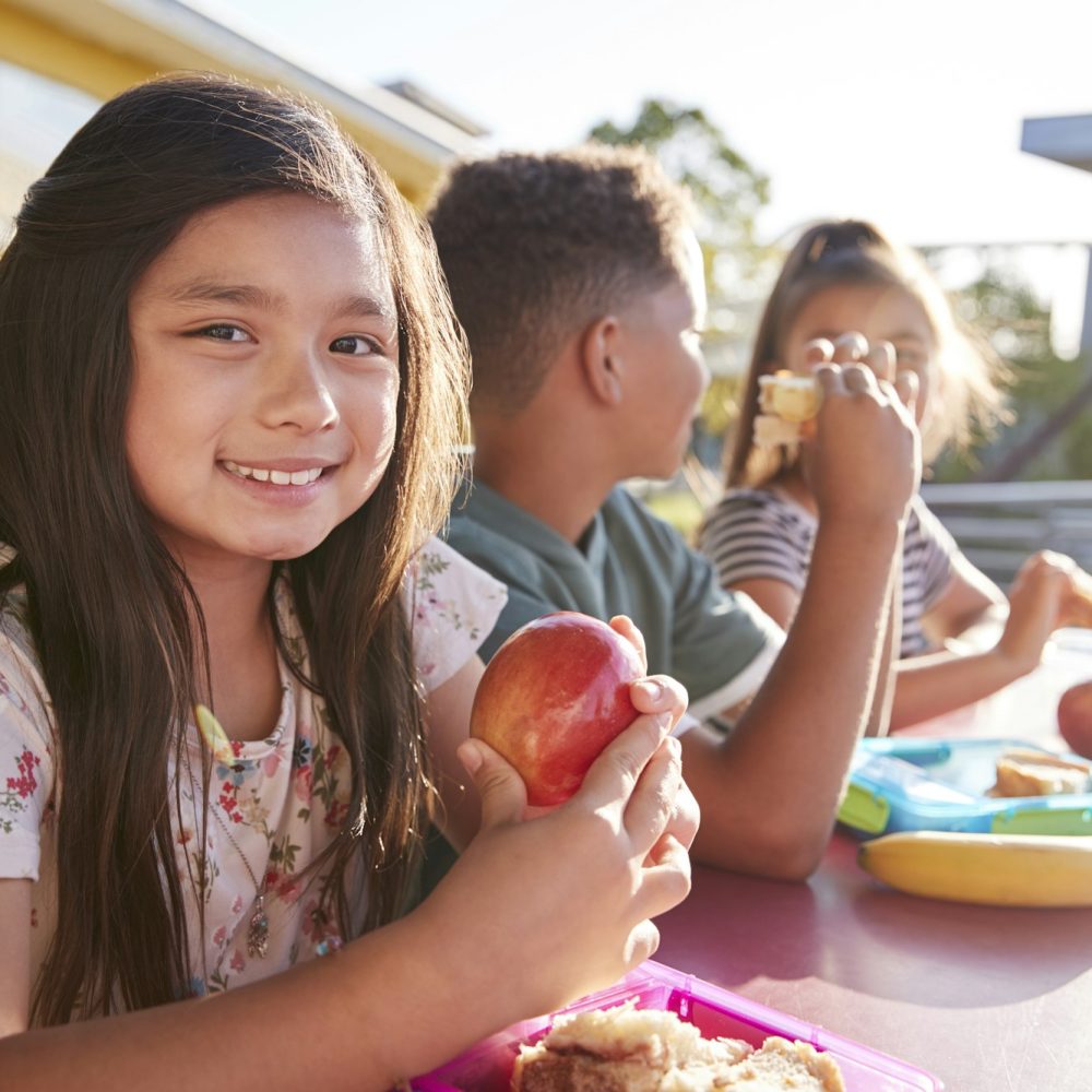 Girl at elementary school lunch table smiling to camera