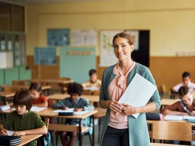 Happy elementary school teacher in the classroom looking at camera.